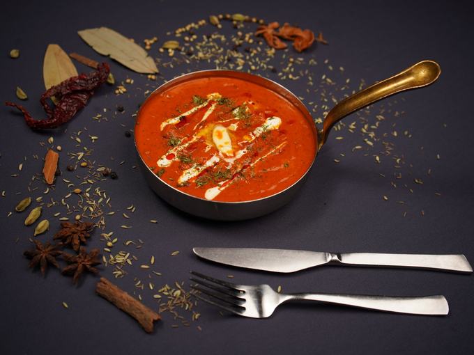 Butter chicken in a copper pan on slate, cream swirled through it, whole spices scattered around.