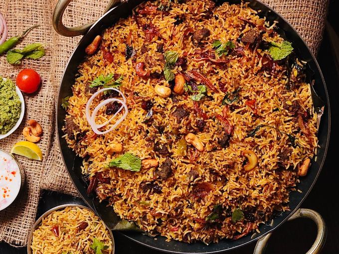 A wide pan of biryani topped with cashews, onion and fresh herbs.