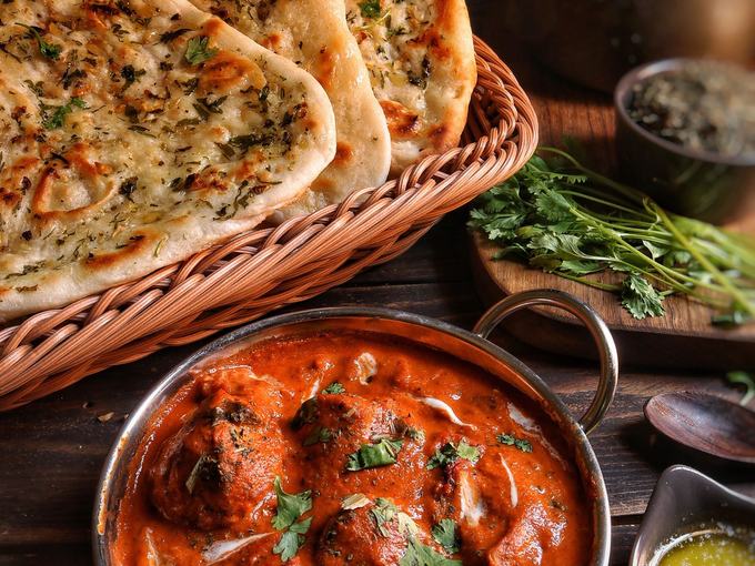 A karahi of rich tomato curry with garlic naan and side dishes.