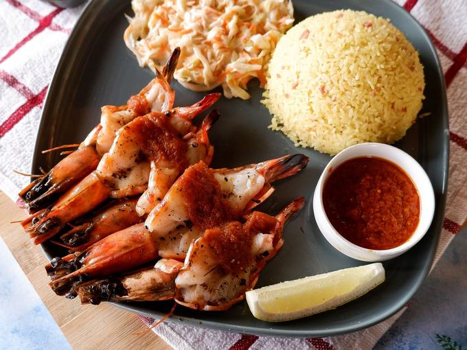 Grilled king prawns served with rice, salad and a pot of sauce.