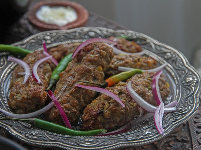 Grilled tikka on a silver platter with raw onion rings and green chilli.