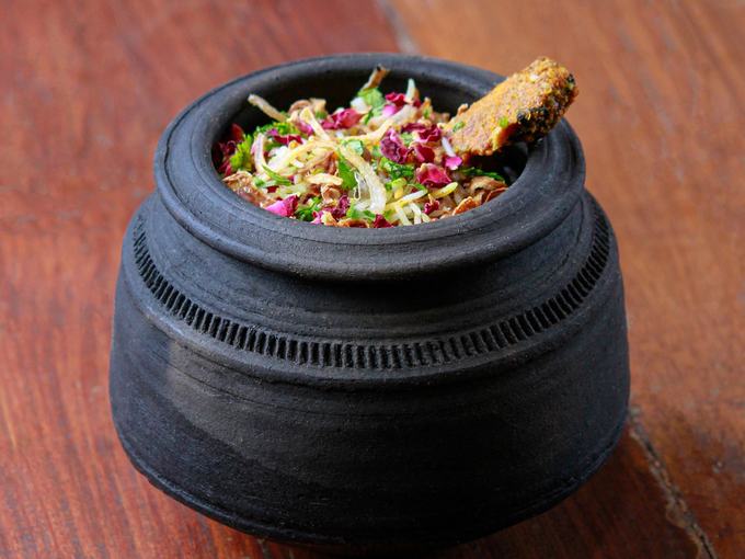 Biryani sealed and served in a black clay handi pot on a wooden table.