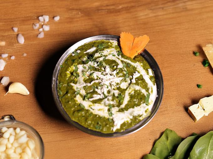 Spinach and paneer curry in a dark bowl on wood, cream swirled on top.