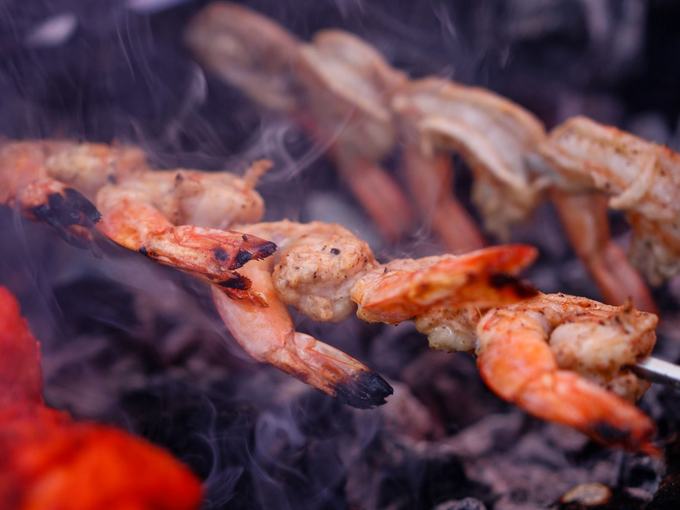 King prawns on skewers over open charcoal, smoke rising off the grill.