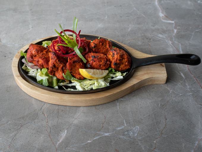 Charred tandoori chicken tikka on a cast-iron paddle with red onion and lemon.