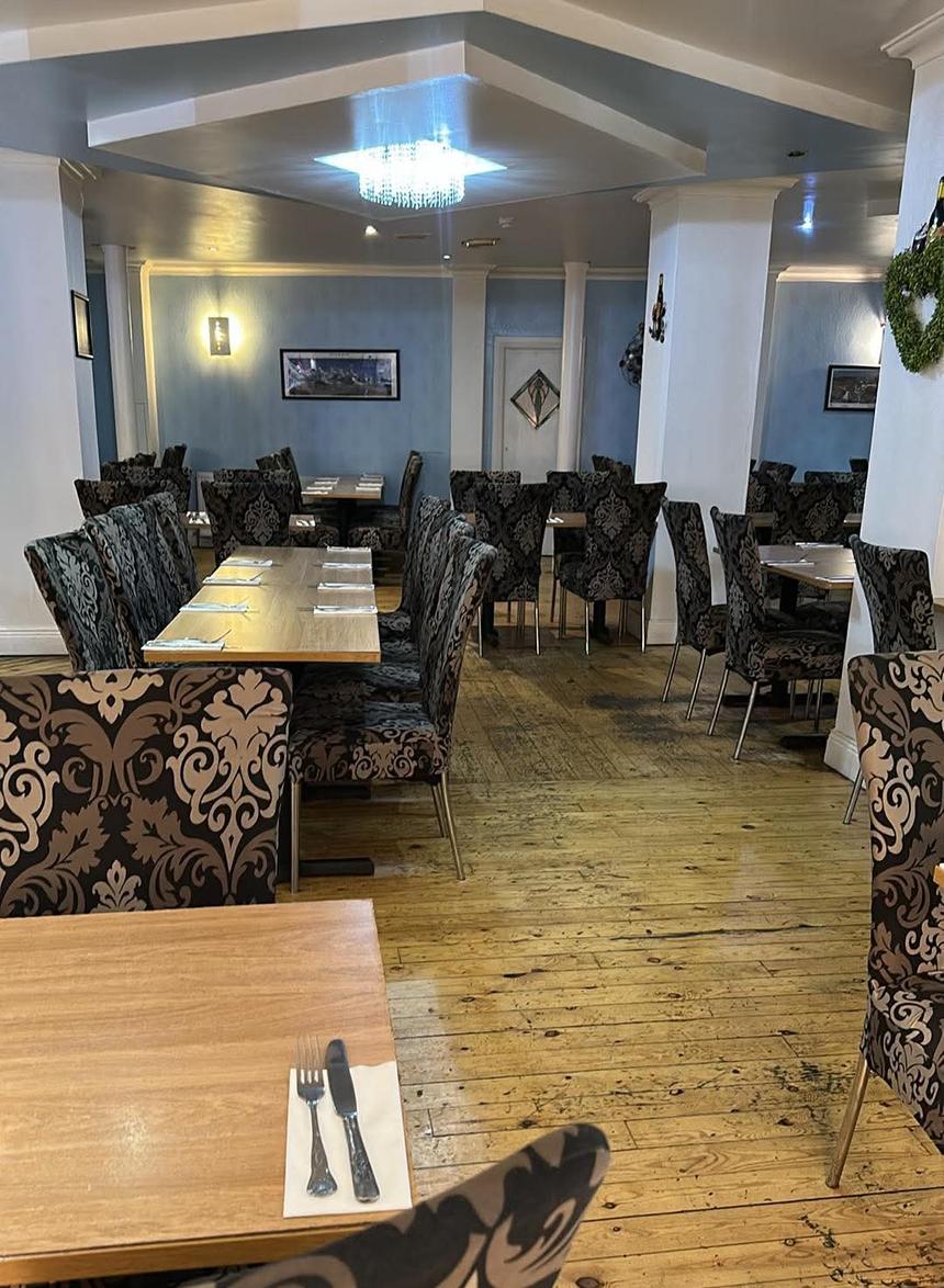 The dining room, tables laid, damask chairs on a wooden floor under a crystal light, blue walls behind.
