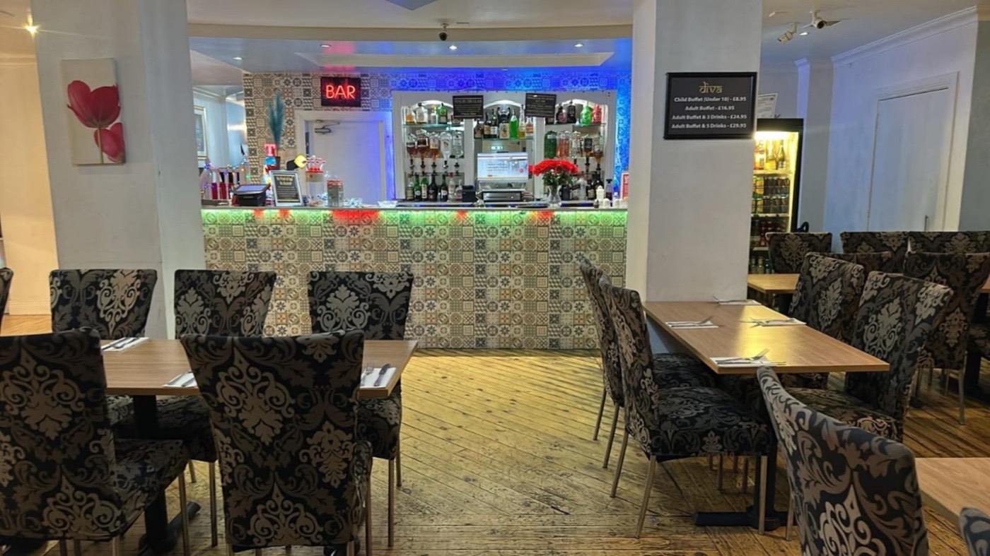 Diva's dining room, tables laid, with the tiled bar lit in blue and green at the far end.